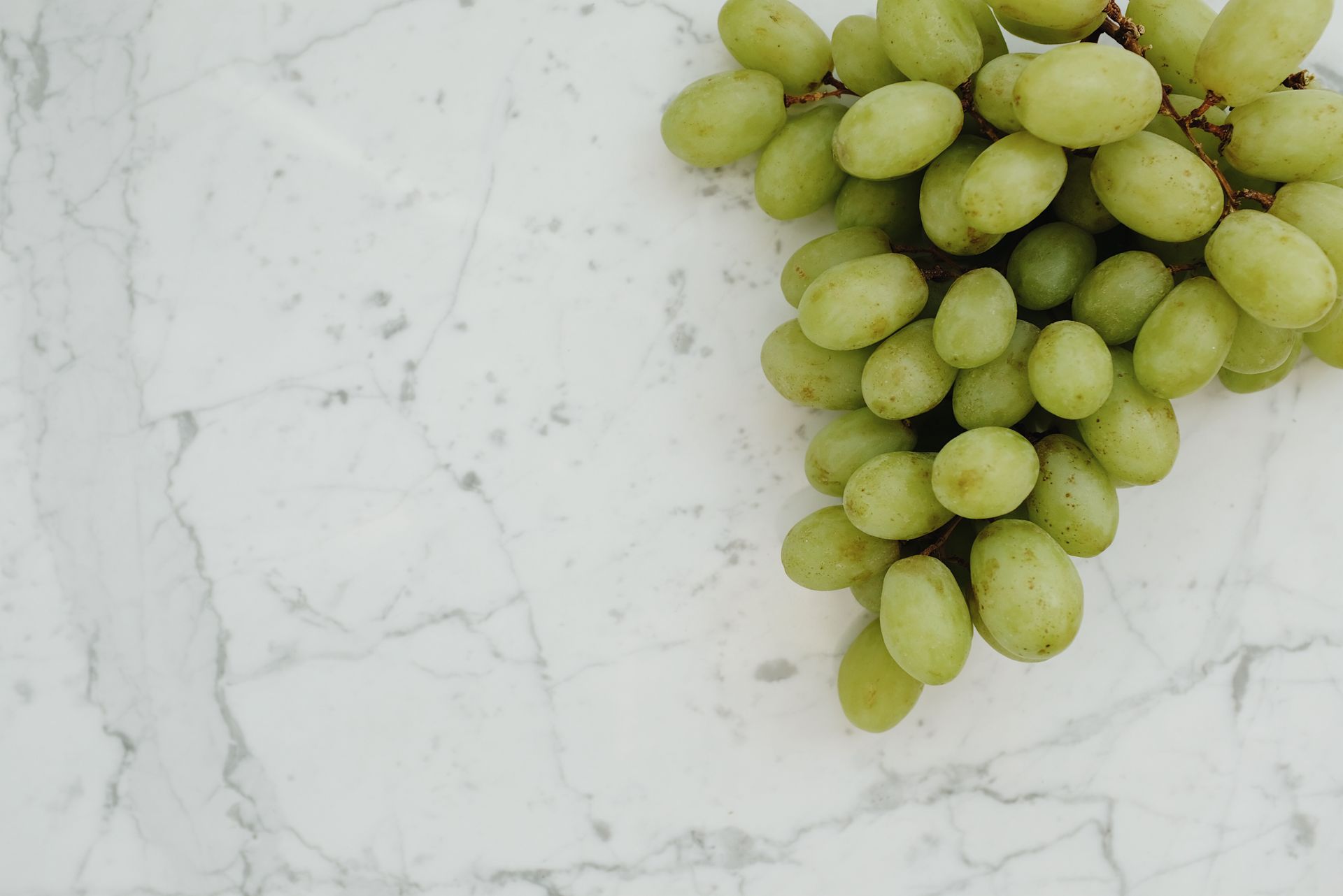 Fresh green grapes clustered on a marble surface